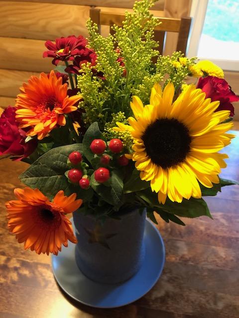 Syksyn väreissä oleva auringonkukkia ja gerberoita sisältävä kukkakimppu maljakossa